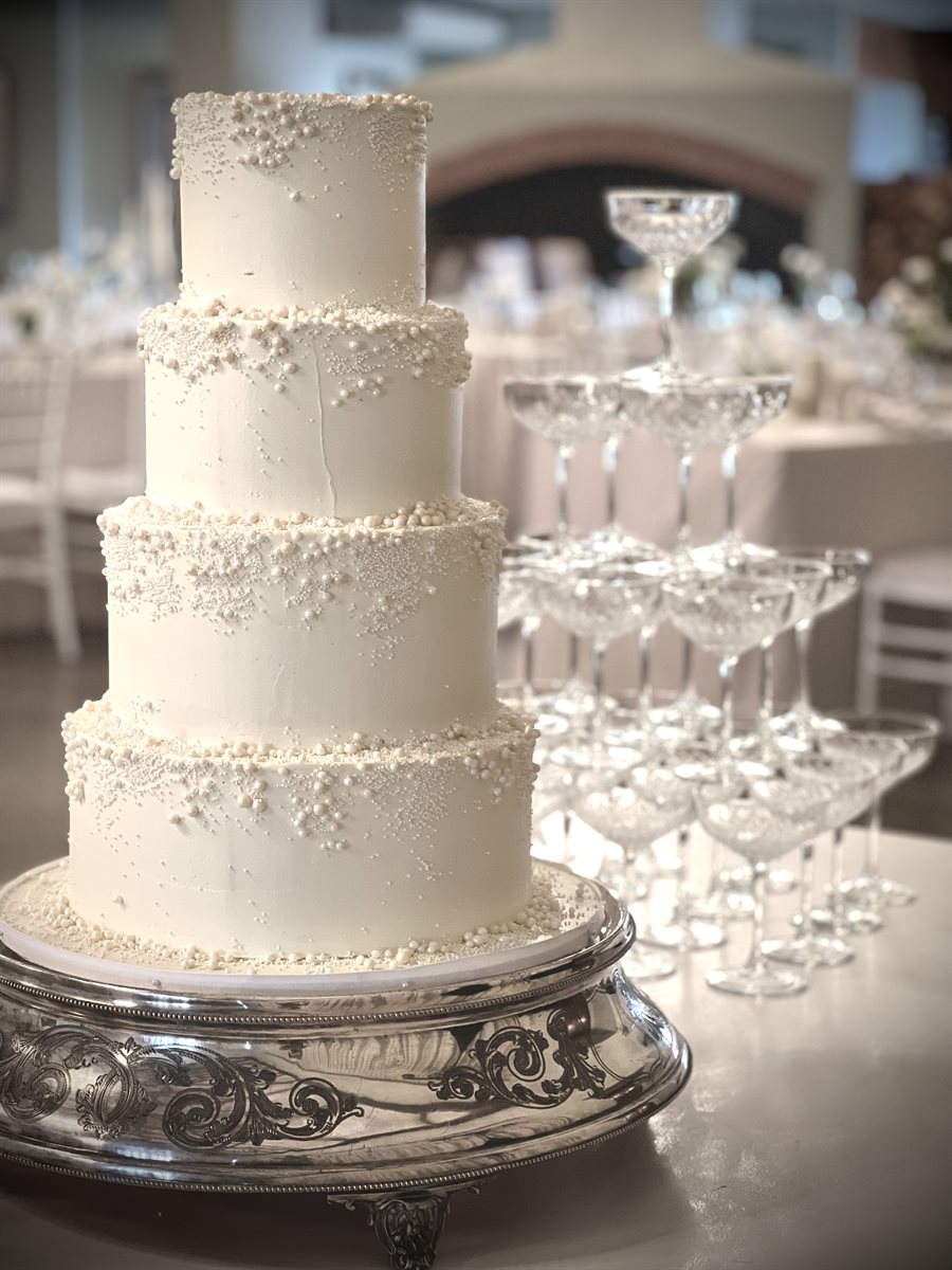 Four-tier white pearl-studded buttercream cake beside a champagne coupe tower