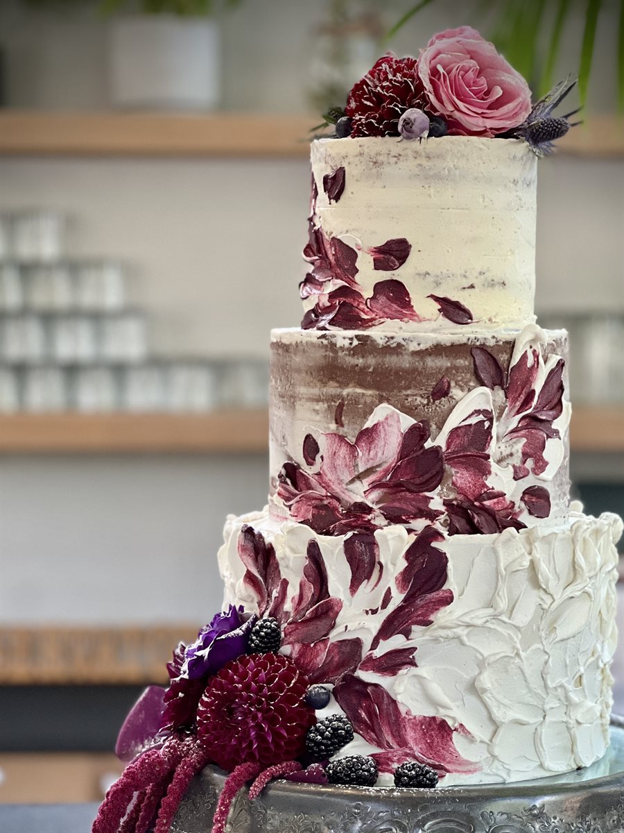 Three-tier painted buttercream cake with hand-painted burgundy and wine brushwork florals, blackberries and purple dahlias