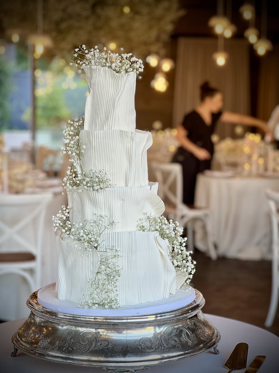 Four-tier pleated ribbed white sugar art cake with fresh gypsophila cascading in pendant-lit reception venue