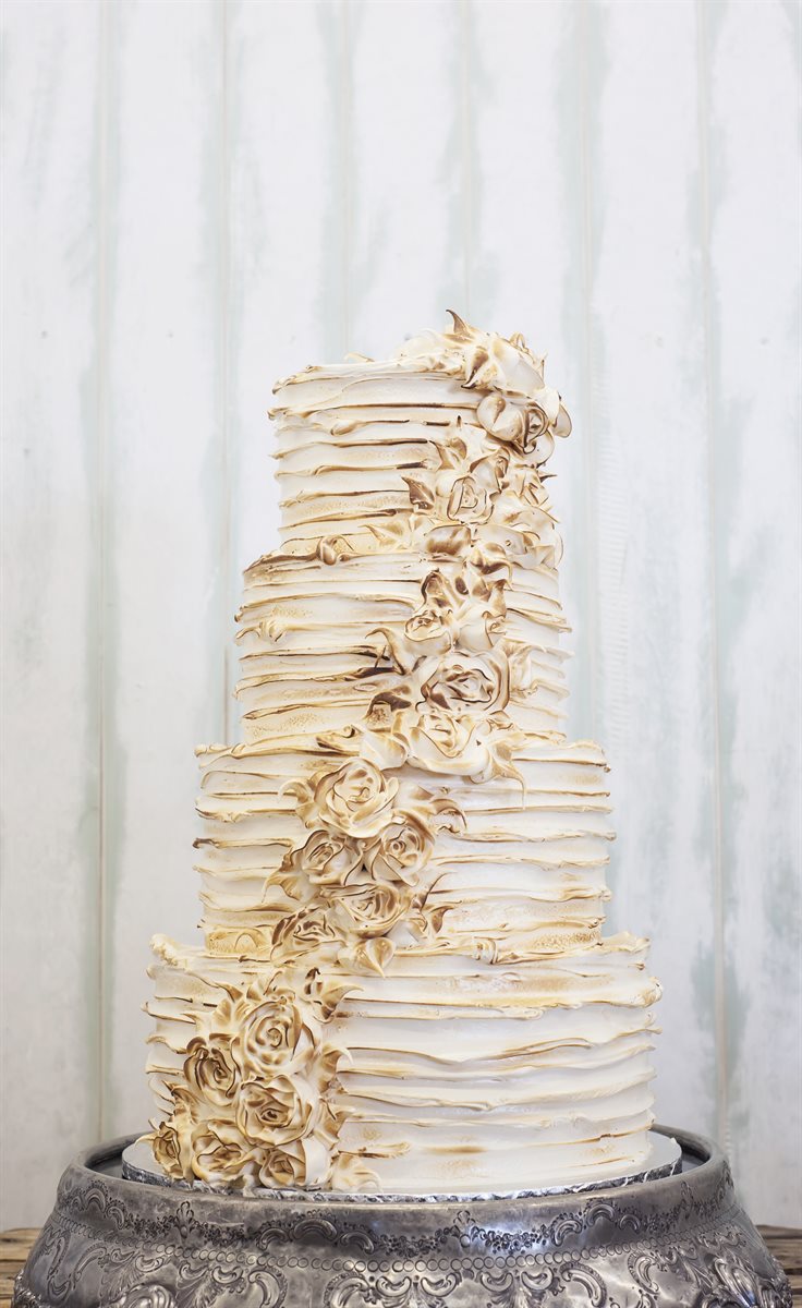 Four-tier toasted meringue cake with golden torched meringue roses cascading down the tiers