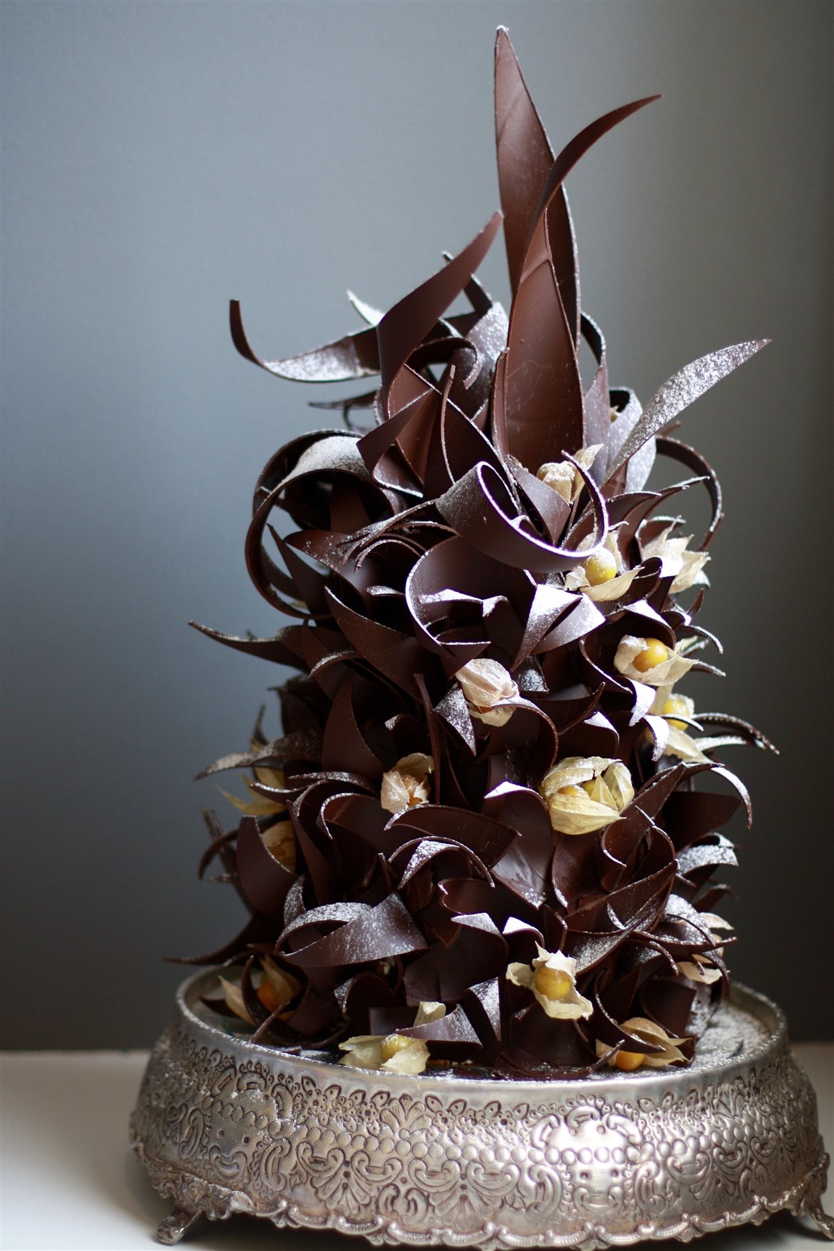 Handcrafted celebration cake — dark chocolate spikey curl tower with cape gooseberry accents by Kanya Hunt