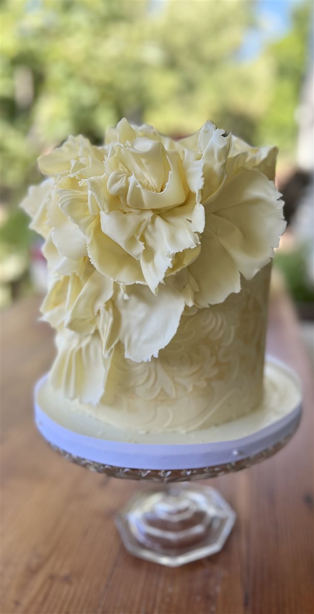 Single-tier white chocolate ruffle flower cake on glass pedestal