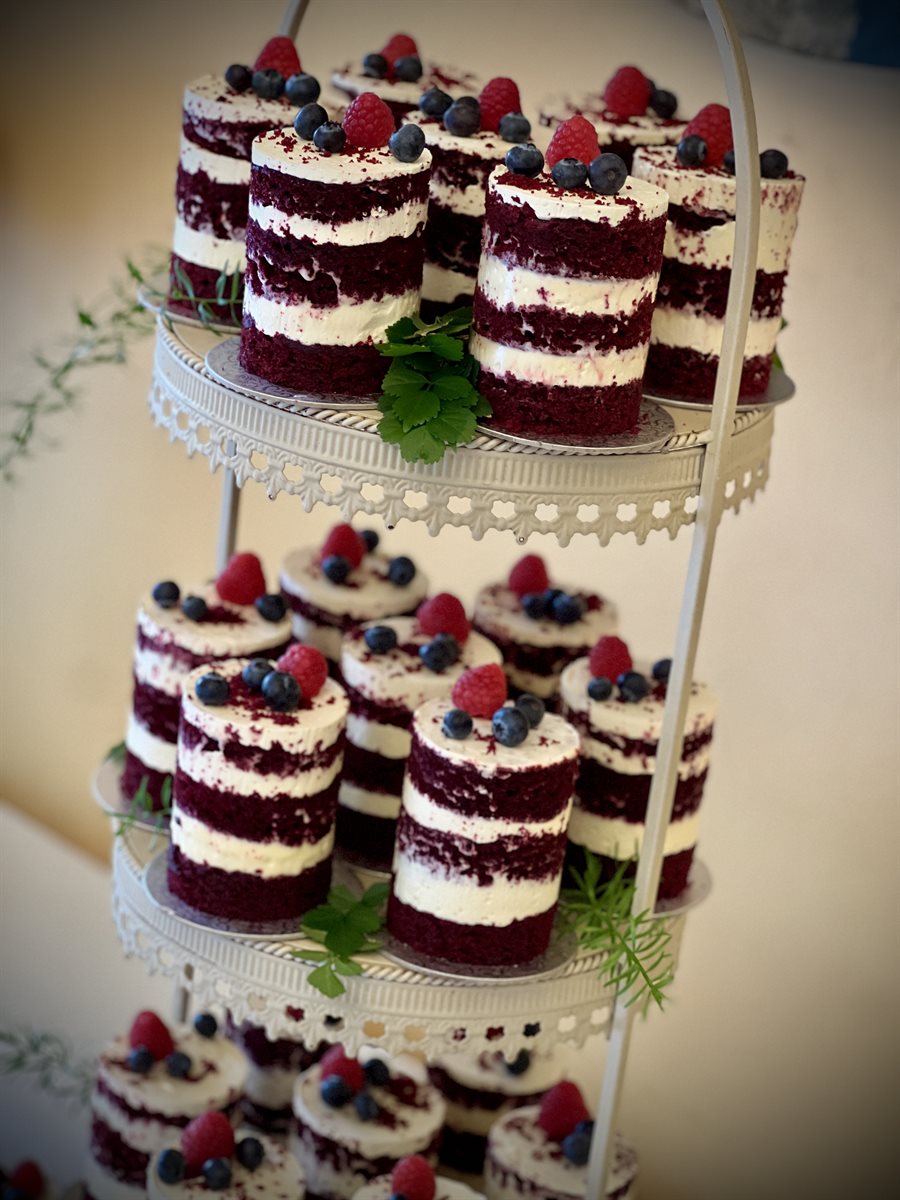 Three-tier cream cake stand of red velvet mini cakes layered with creamcheese buttercream and topped with raspberries and blueberries — a petite tower display
