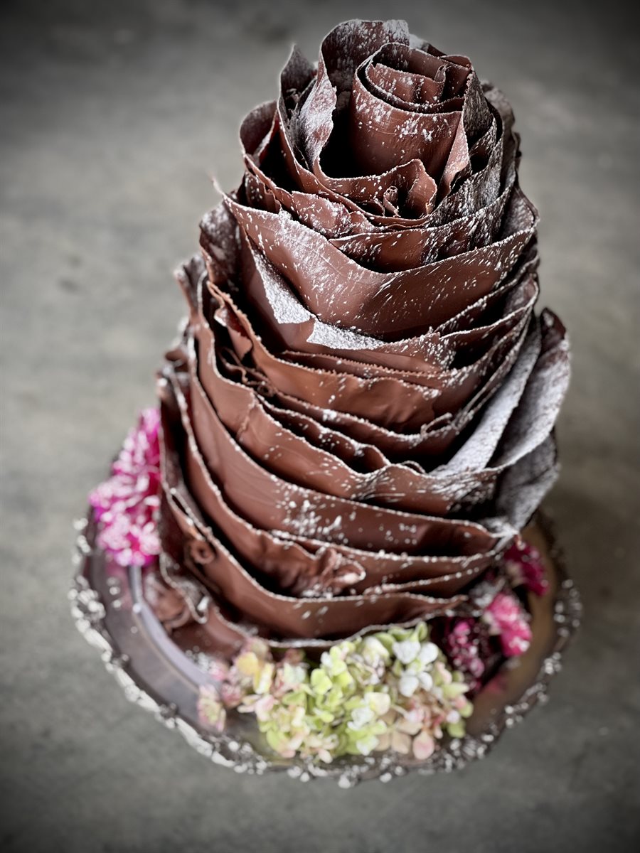 Aerial view of a tiered chocolate tower cake dusted in icing sugar on a silver cake stand