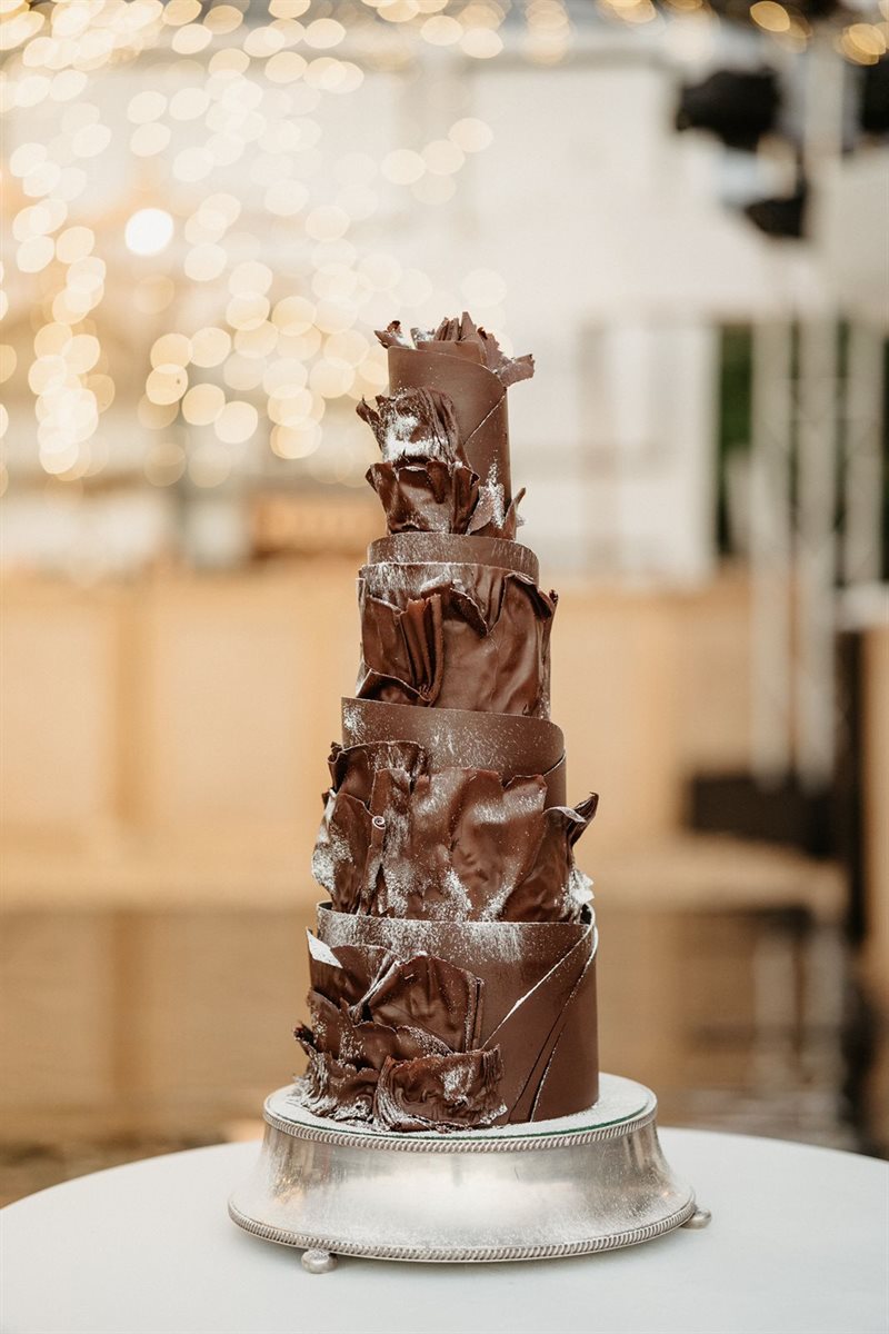 Tall contemporary chocolate collar cake on silver pedestal with fairy light bokeh