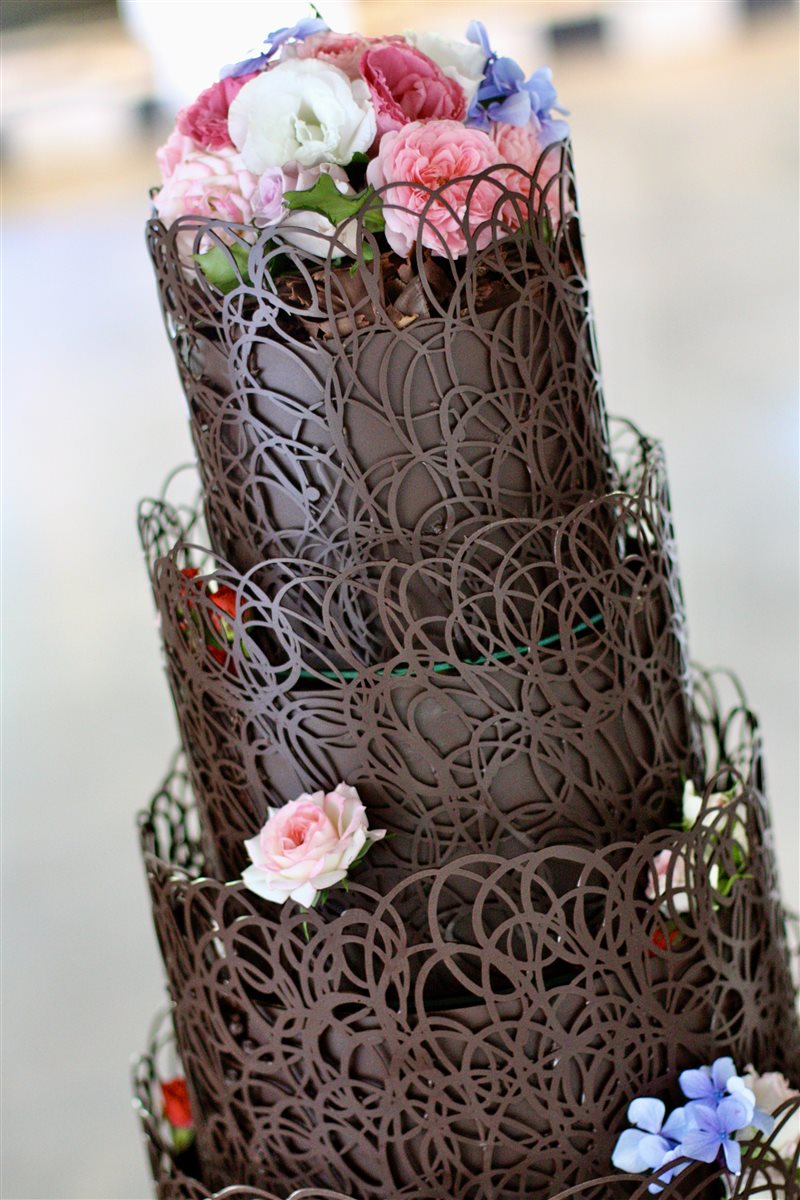 Three-tier dark chocolate filigree lattice cake with pink roses and blue hydrangeas