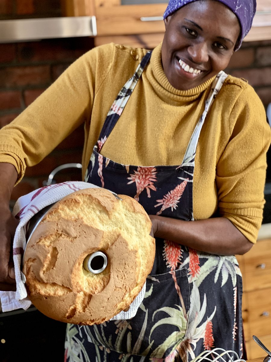 One of Kanya's team (our head baker, Winkie or Thandeka as is her Xhosa name) — apron on, bundt cake in hand, warm kitchen light
