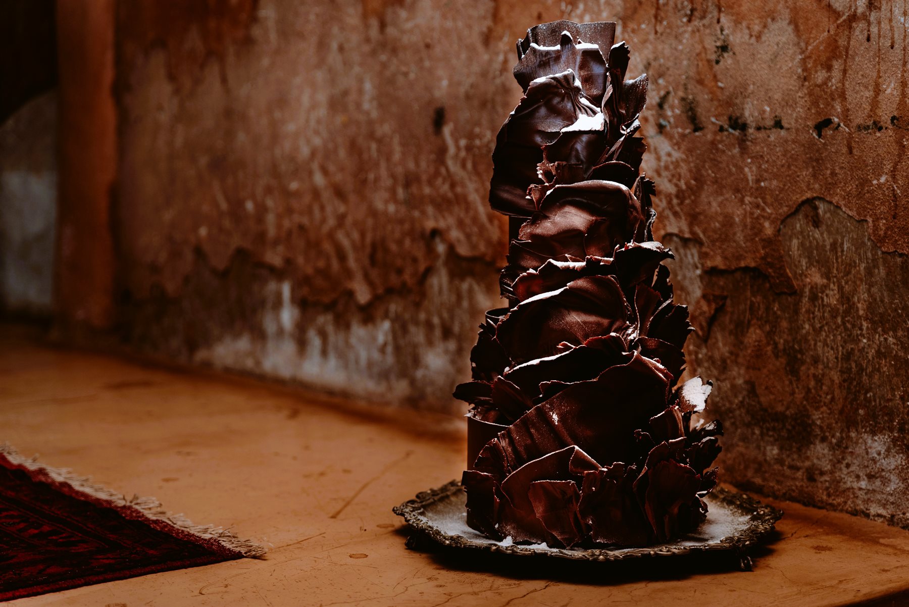 Hand-sculpted tower of dark couverture chocolate flowers against a moody terracotta wall