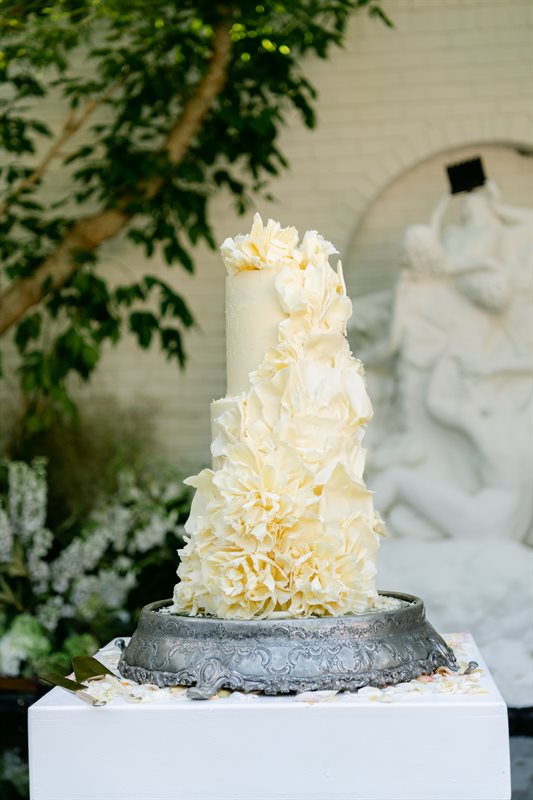 Tall ivory white couverture wedding cake with cascading ruffles on antique silver pedestal