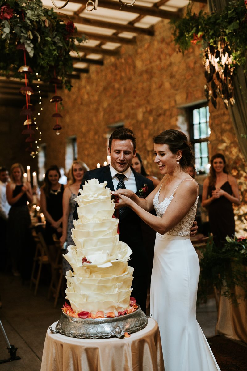 Romantic cake-cutting moment in a rustic Cape barn, couverture chocolate cake with wild florals