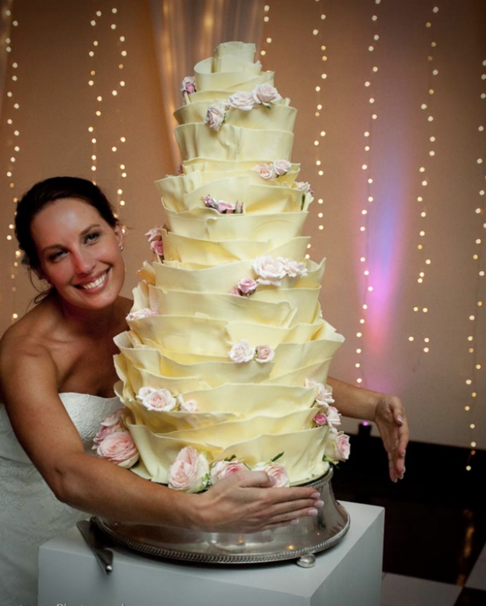 Bride embracing a tall multi-tier white couverture ruffle cake with blush pink garden roses