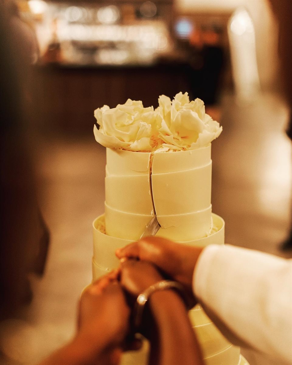 Close-up of the couple's hands cutting through white chocolate rose couverture wedding cake