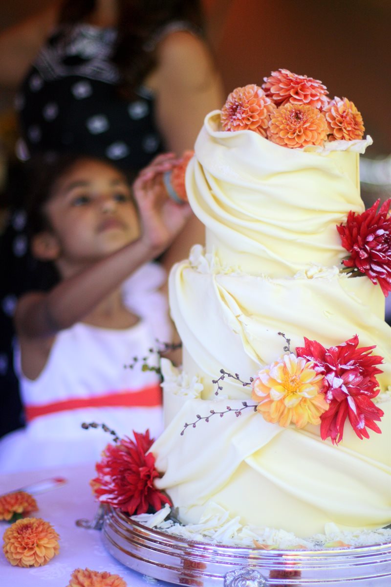 Tiered white couverture cake with draped panels and a cascade of orange and red dahlia blooms