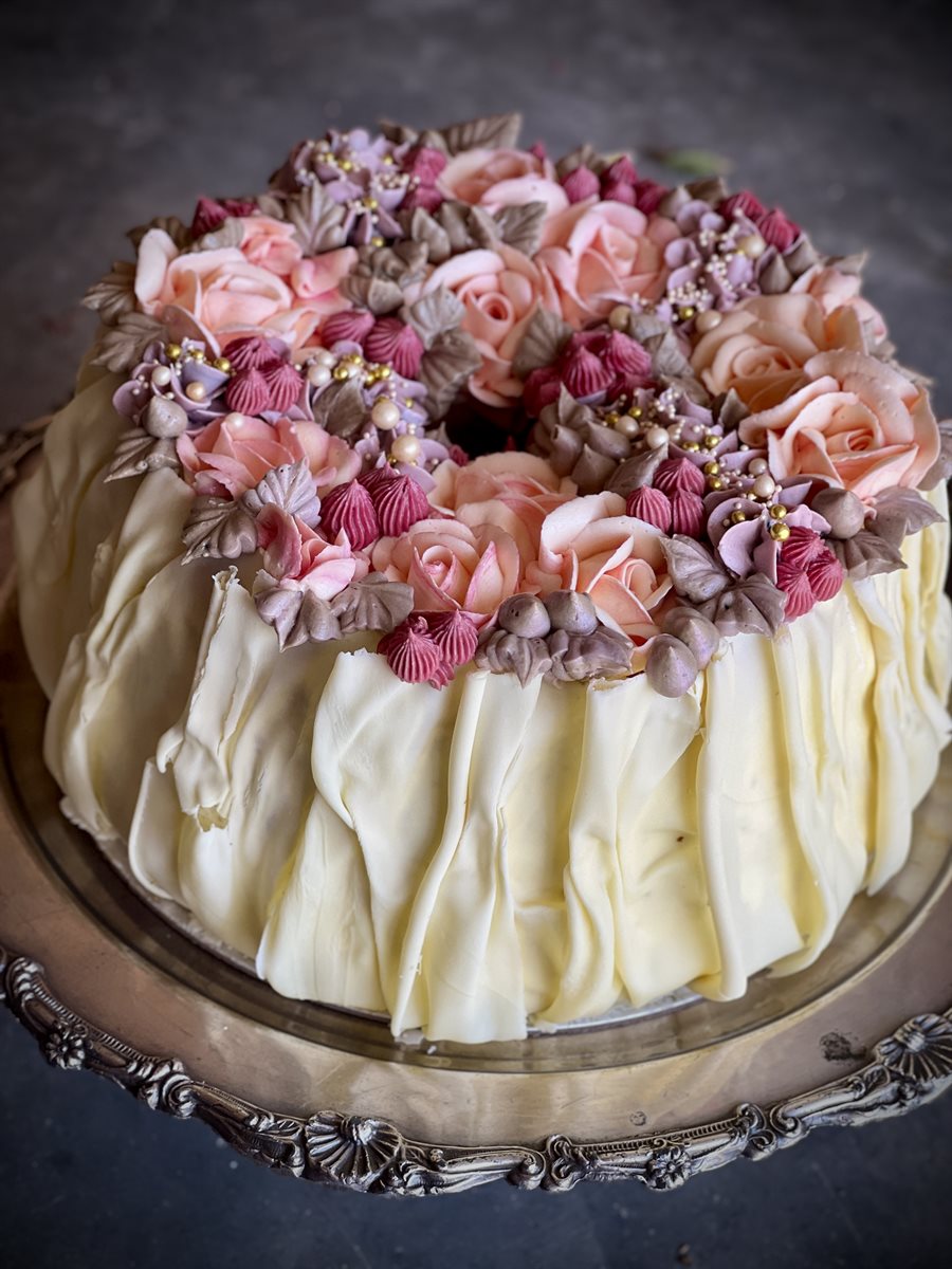 Chiffon cake with white chocolate ruffled sides crowned with a wreath of piped peach roses, mauve hydrangeas and mocha leaves with gold pearl accents, on an ornate silver tray