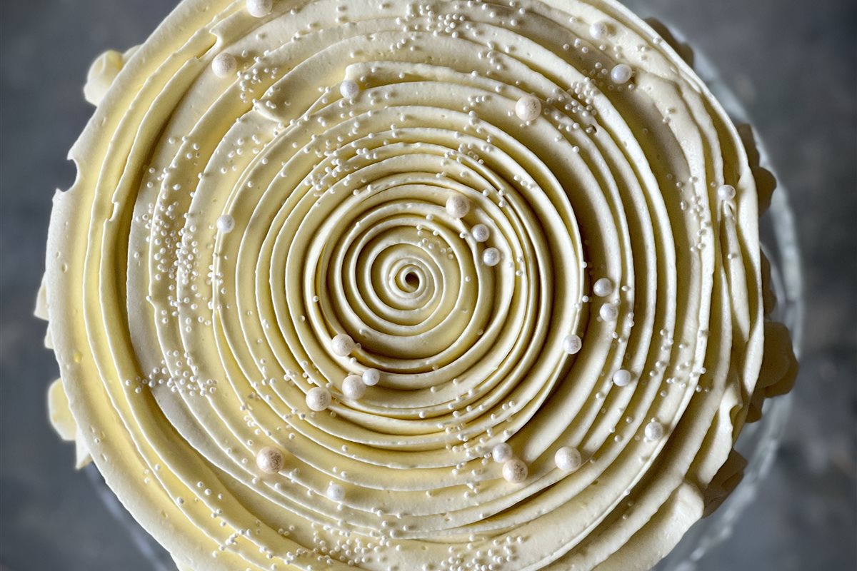 Aerial view of a cake with a perfect concentric spiral piped in ivory buttercream and pearl sugar beads