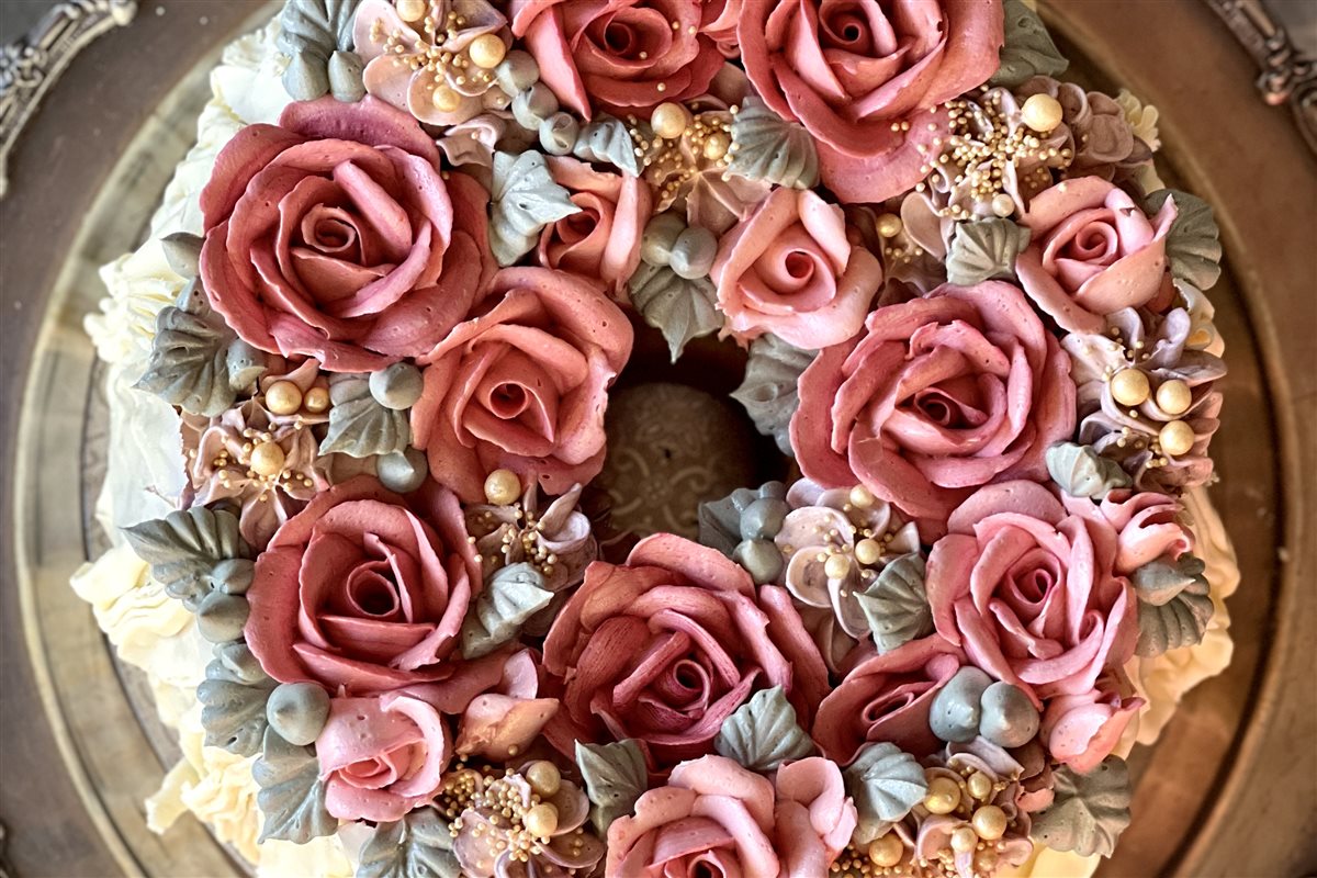 Aerial view of chiffon ring cake with wreath of dusty mauve-rose buttercream roses and gold pearls