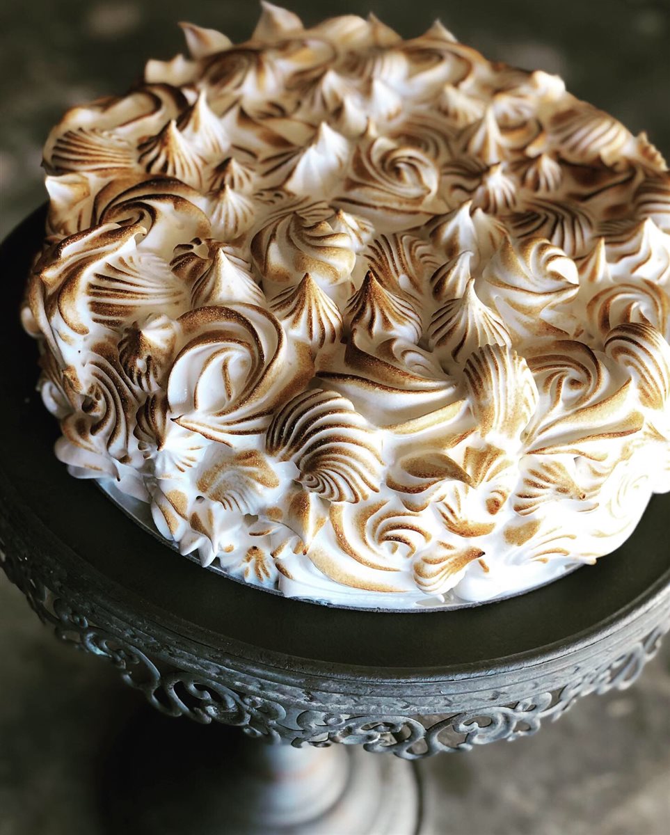 Single-tier cake entirely covered in swirled torched meringue peaks, on a vintage dark pewter stand