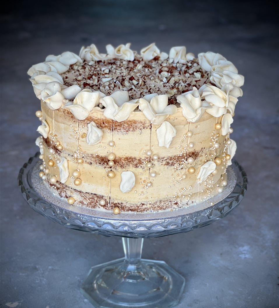 Moca cake with caramel and walnuts and piped buttercream flowers, on a crystal glass cake stand
