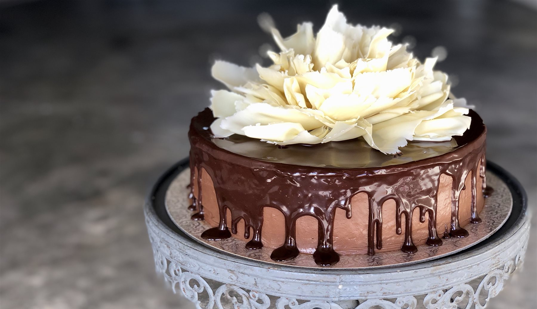 Belgian chocolate mousse cake with a glossy chocolate ganache drip, topped with a large sculpted white couverture chocolate bloom