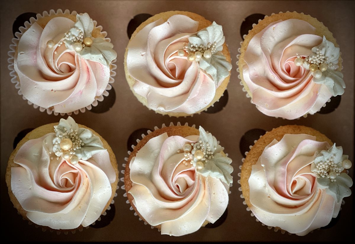 Six cupcakes in a presentation box — pale blush buttercream rose swirls with white sugar-flower clusters