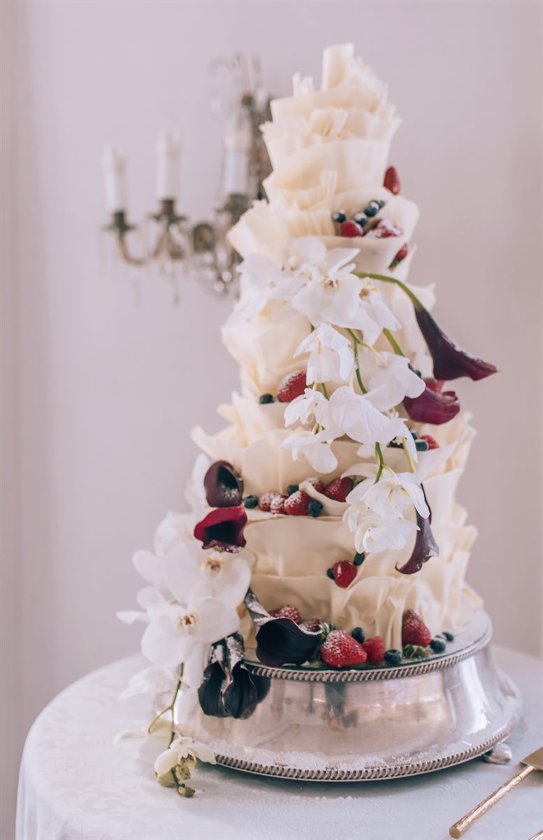 Multi-tier white ruffle cake with white orchids, dark calla lilies and fresh berries