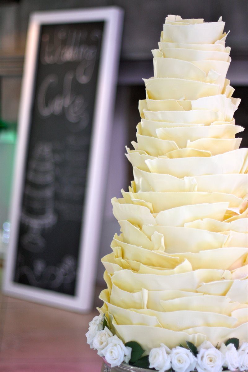 Conical white chocolate petal spiral cake with white garden roses at base and chalkboard backdrop