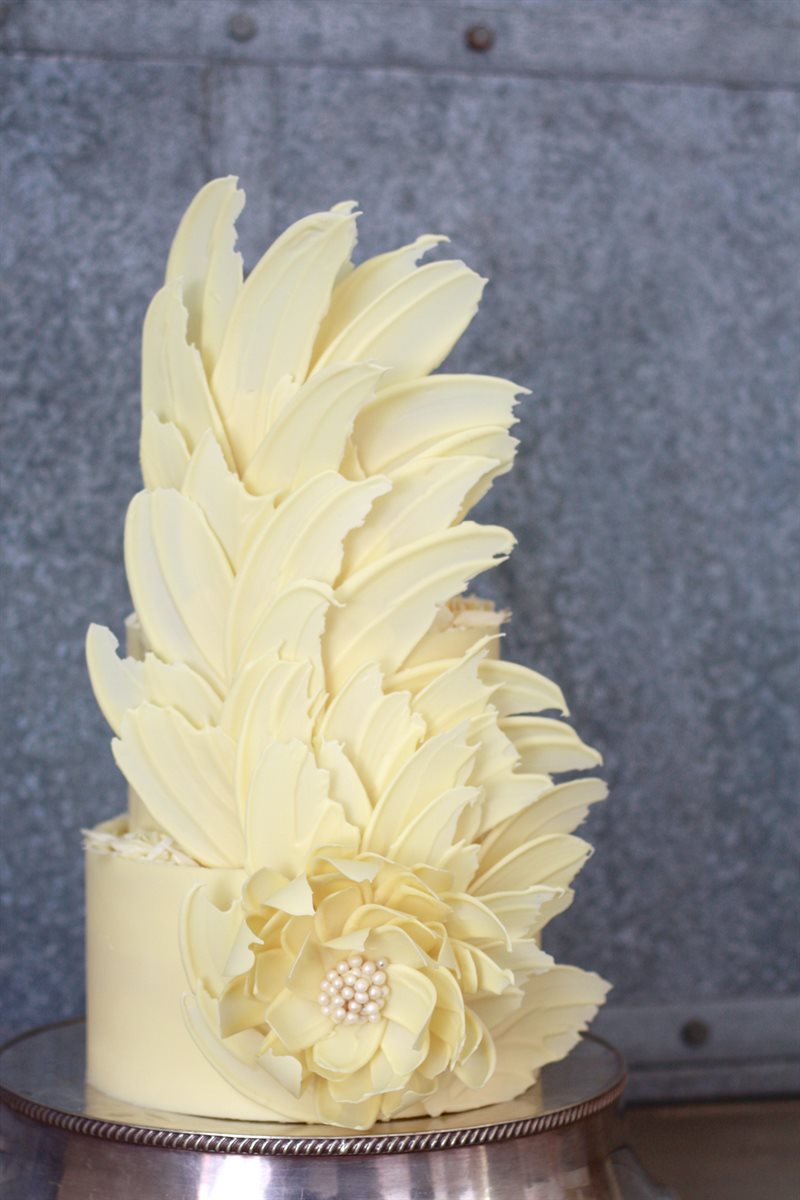 White chocolate feather plume rising dramatically from three-tier cake with a sculpted pearl-centred flower