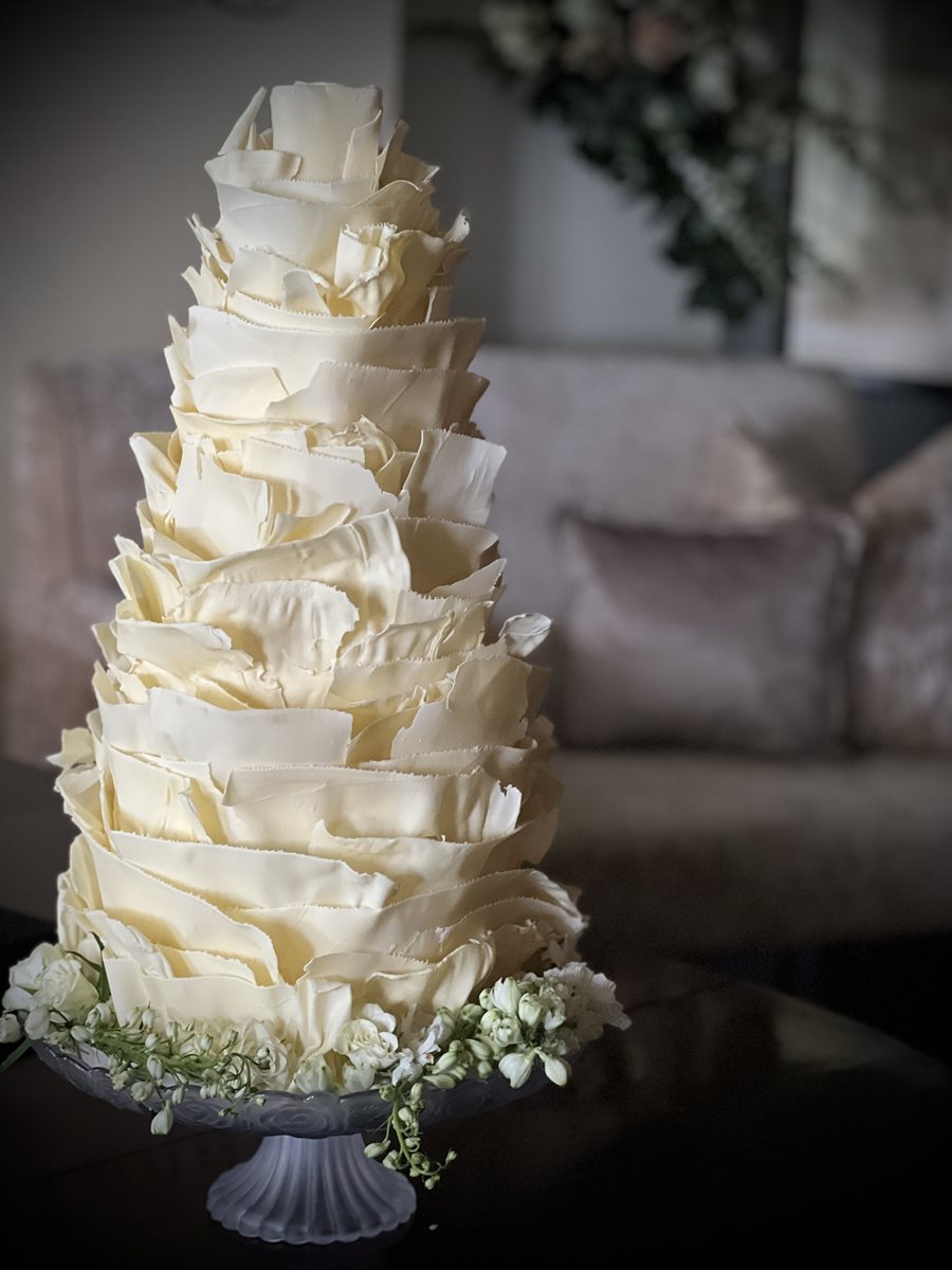 Three-tier white chocolate tower cake on white stand with soft blurred interior background