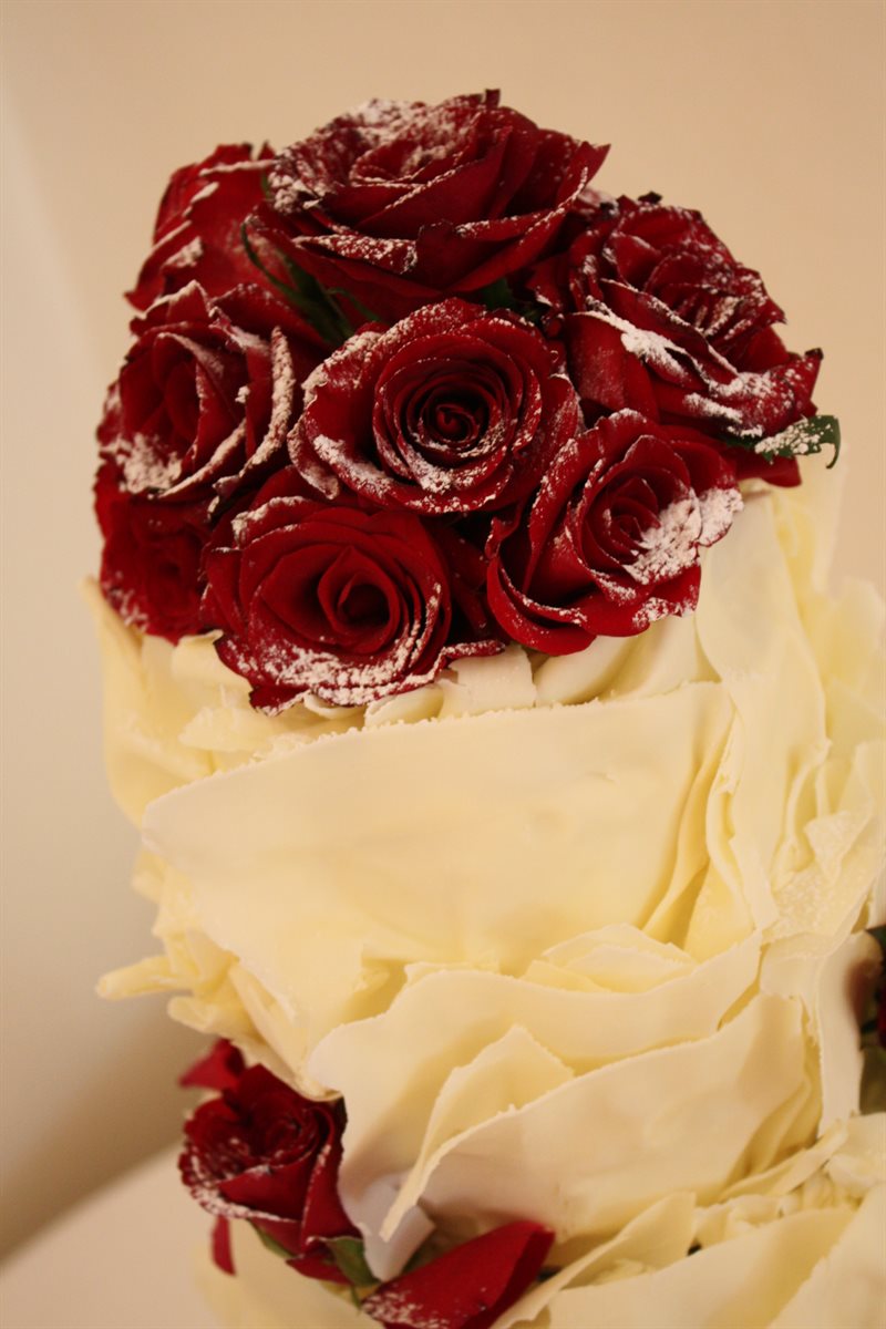 Detail of white couverture ruffle cake topped with icing-sugar-dusted crimson roses